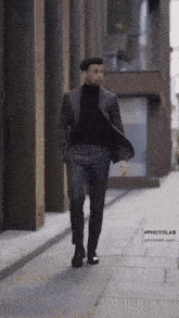 a man in a suit and black turtleneck is walking down the street .