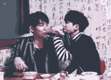 two young men are sitting at a table eating food and drinking wine