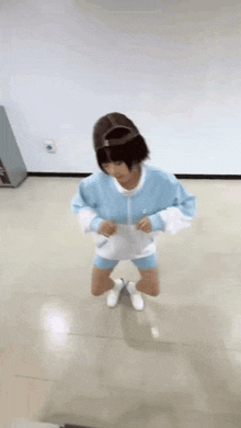 a woman in a blue jacket and shorts is kneeling down on the floor .