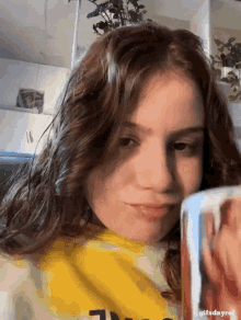 a girl in a yellow shirt is looking at a mug with a picture of a person on it
