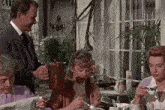 a group of people are sitting at a table eating and drinking tea