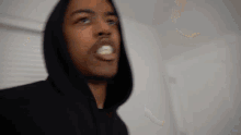 a man in a black hoodie is making a funny face while standing in a room .