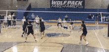 a group of people are playing volleyball in front of a sign that says wolf pack fans family