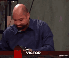 a bald man with a beard is laughing while sitting at a table with a red x on it .