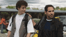a man in a black jacket stands next to a boy with a backpack on his back