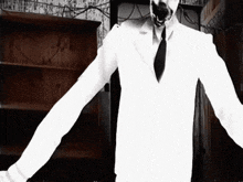 a man in a white suit and tie is standing in a dark room with his arms outstretched