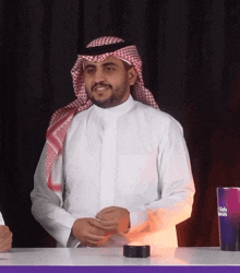 a man wearing a white shirt and a head scarf is sitting at a table with a cup that says dubai on it
