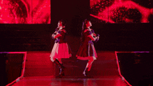 two women are dancing on a stage in front of a red background