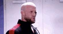 a bald man with a beard is standing in a locker room looking at the camera .