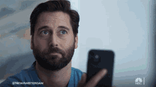 a man with a beard is looking at a cell phone with the nbc logo on the bottom
