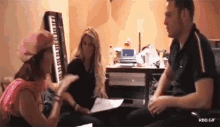 a group of people are sitting in a room with a keyboard in the background .