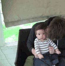 a man is holding a baby in his lap and kissing it
