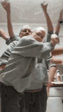 two men are dancing in a kitchen with their hands in the air .