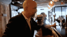 a bald man with a beard is holding a glass of beer in a bar .