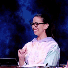 a woman wearing glasses and a tie dye hoodie smiles