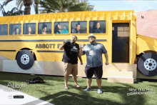 two men are standing in front of a large yellow school bus that says abbott elementary
