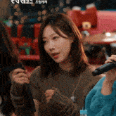 a woman in a brown sweater holds a microphone in her hand