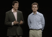 a man in a suit is pointing at another man in a blue shirt on a stage