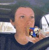 a woman is eating a sandwich in a car while holding a mug with a picture of a character on it .
