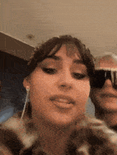 a close up of a woman 's face with a man behind her wearing sunglasses