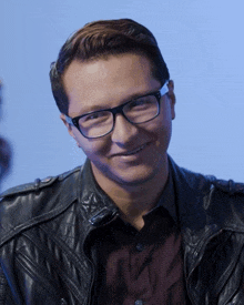 a man wearing glasses and a black leather jacket smiles