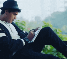 a man wearing a hat and a watch sits on a bench writing in a notebook