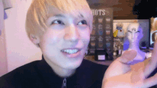 a man with blonde hair is smiling in front of a sign that says hots