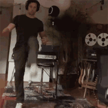 a man wearing headphones is playing a guitar in a room with tape reels on the floor .