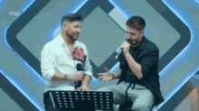 two men singing in front of a microphone with rtve in the background