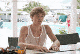 a man in a wet tank top sits at a table in front of a pool with the words things that make sa happy above him
