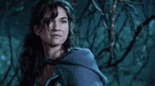 a woman in a blue cape stands in a forest