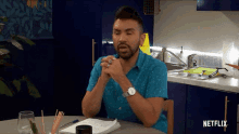 a man in a blue shirt is sitting at a table with a netflix logo on the bottom
