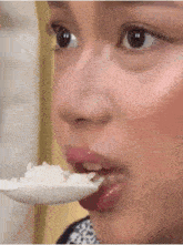 a close up of a woman eating rice from a white spoon
