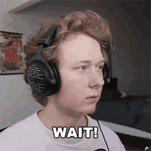 a young man wearing headphones and a white shirt says wait .