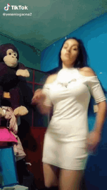 a woman in a white dress is dancing with a stuffed monkey in the background