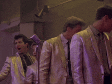a group of men singing into microphones while wearing gold suits