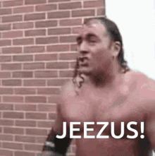 a shirtless man is standing in front of a brick wall and says jeezus