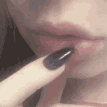 a woman with black nails is touching her lips with her finger .