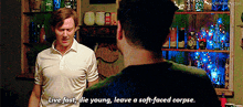 two men are standing next to each other and one of them is saying live fast die young leave a soft faced corpse