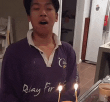 a man wearing a purple shirt that says pray for is blowing out candles on a cake
