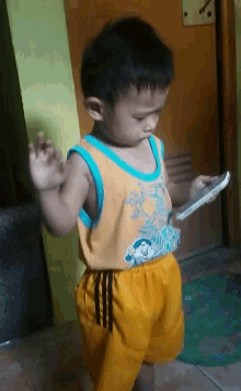a young boy in a yellow tank top and yellow shorts is playing with a cell phone