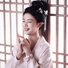 a woman wearing a white kimono is smiling with her eyes closed and her hands folded