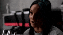 a woman with blue hair is sitting in a chair in a dark room and talking to someone .