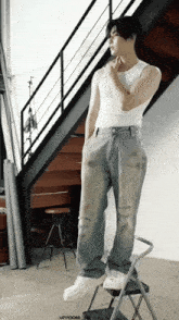 a man in a white tank top stands on a step ladder