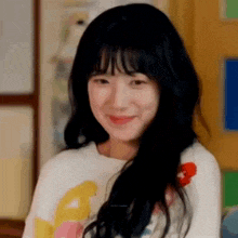 a woman with long black hair is smiling and wearing a white shirt .