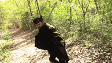 a man wearing a black cape and a crown walks down a path in the woods