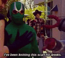 a man in a green costume is talking about knitting a scarf