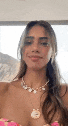 a woman wearing a necklace and a pink top is smiling and looking at the camera .
