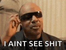 a bald man wearing sunglasses is talking on a cell phone and saying `` i ain t see shit '' .
