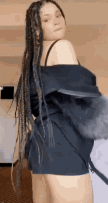 a woman with braids is standing in a room wearing a black shirt and shorts .